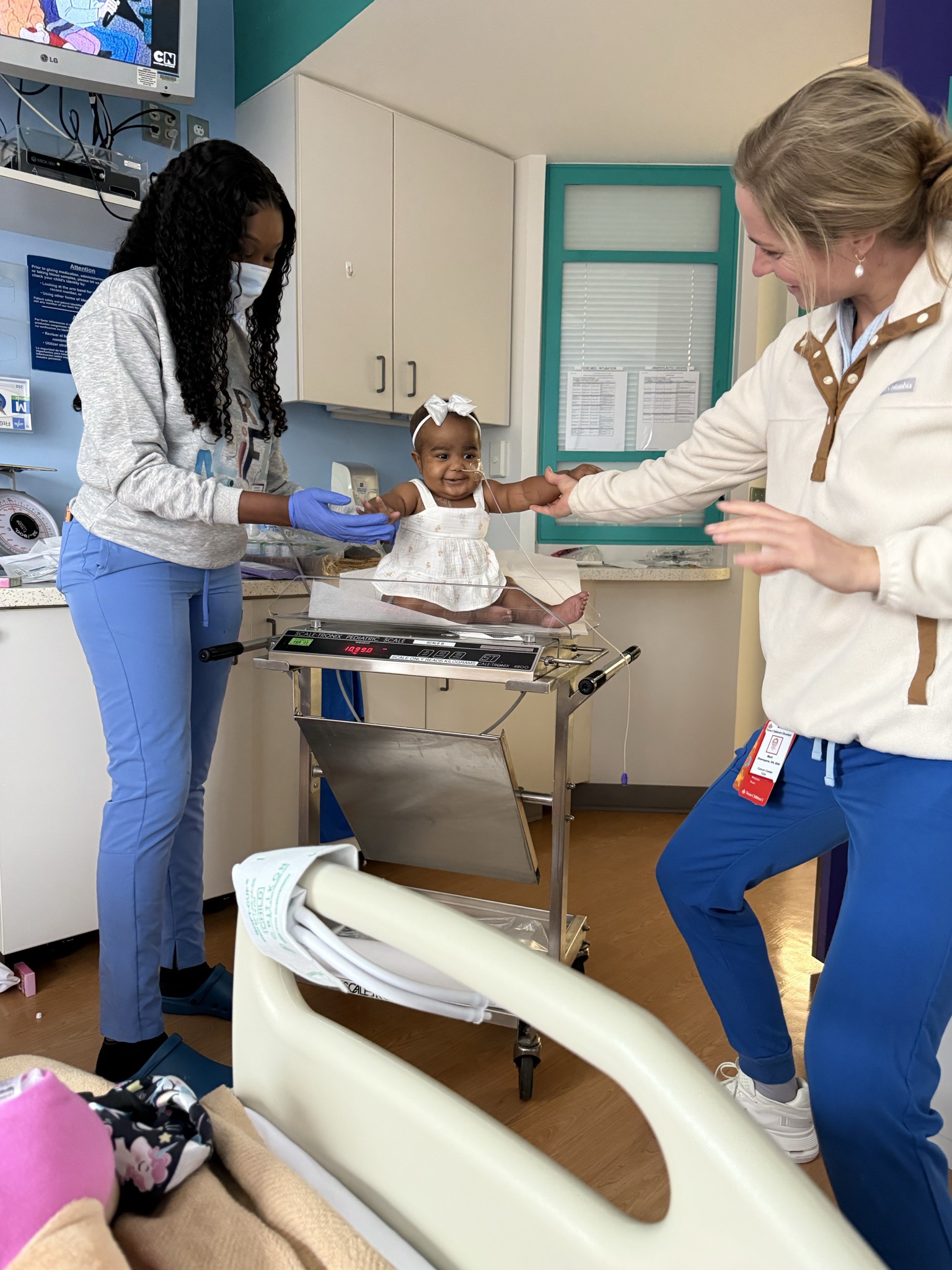 Kylin smiling on a clinic examination table as medical care team members at Texas Children's Hospital interact with her.